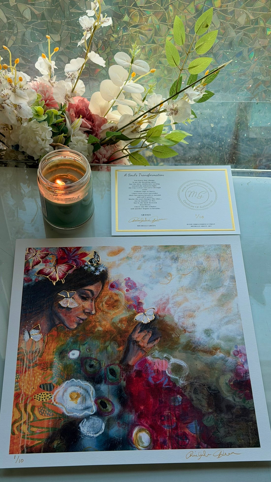 Art print of a woman with flowers, a candle, and a card on a glass table.