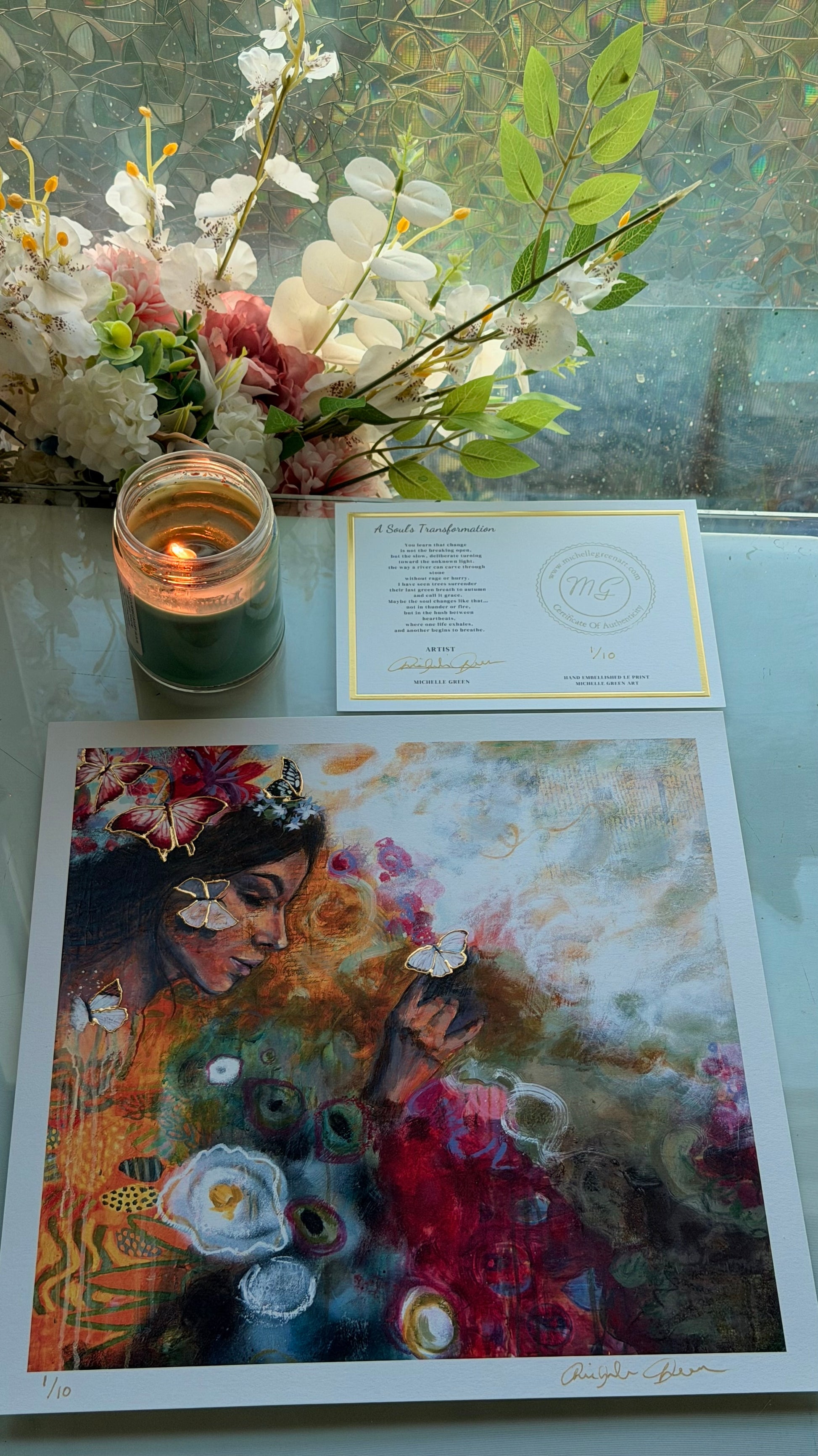 Art print of a woman with flowers, a candle, and a card on a glass table.