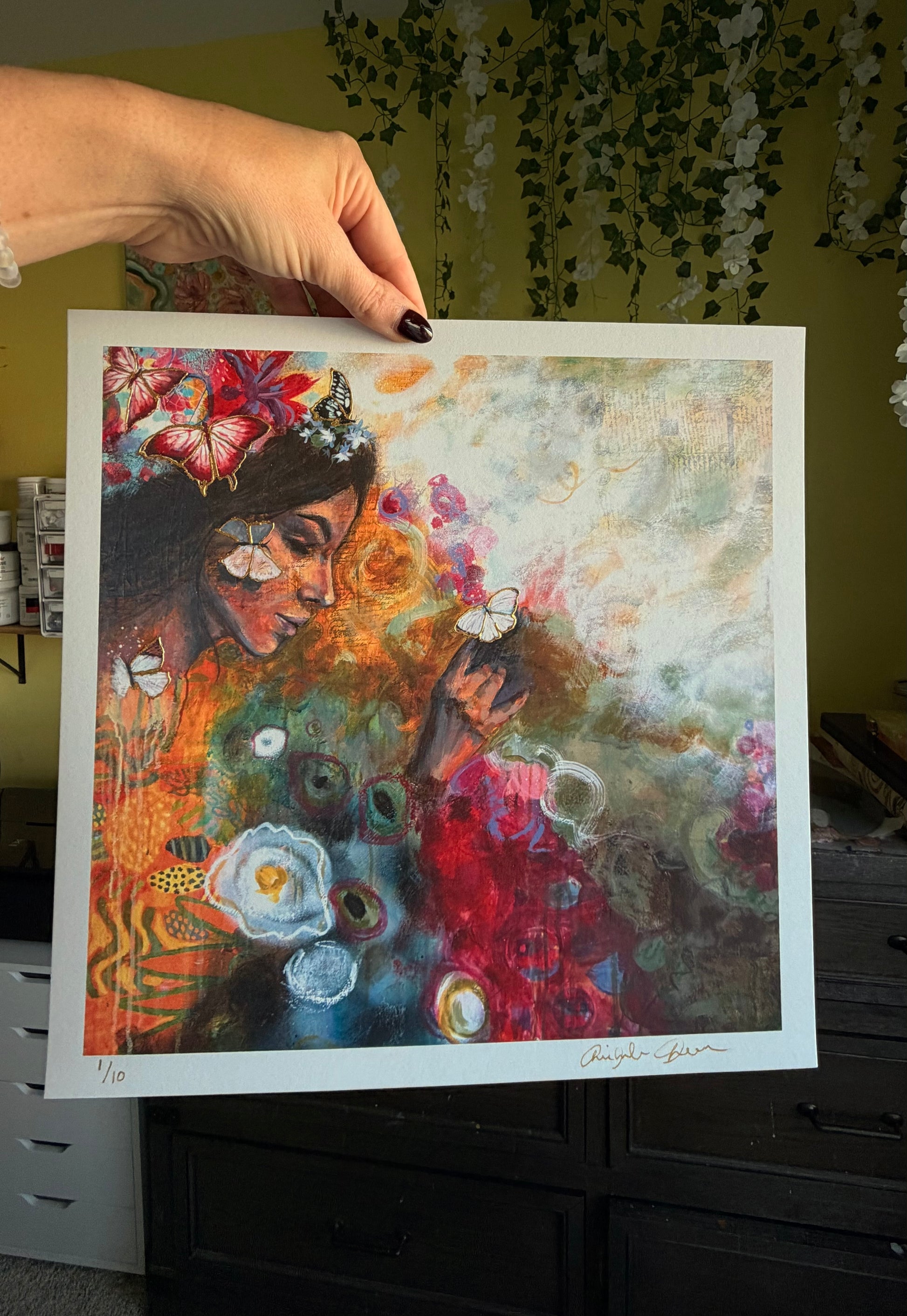 Colorful artwork of a woman with flowers held by a hand against a neutral background