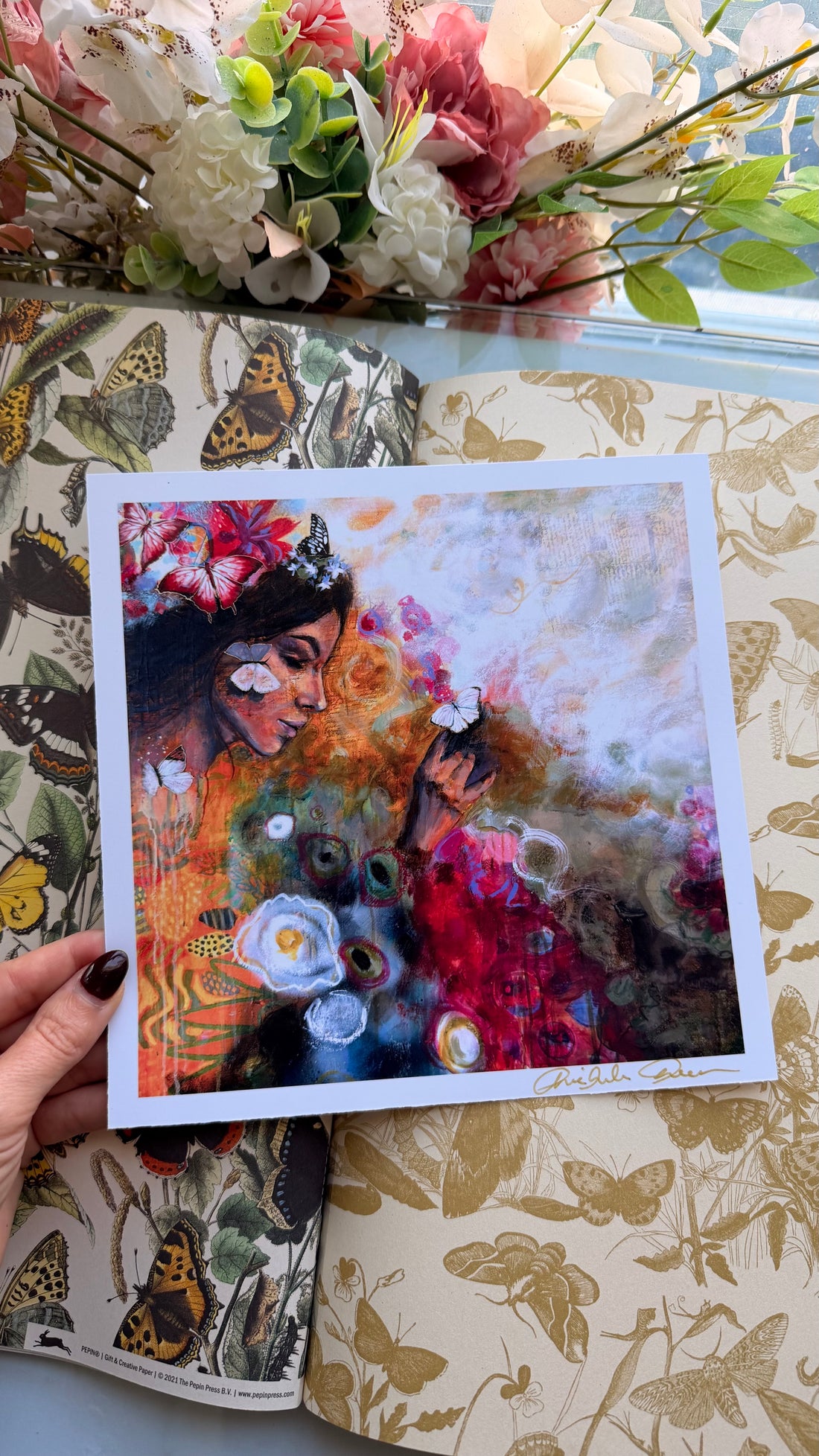 Hand holding a colorful painting of a woman with flowers