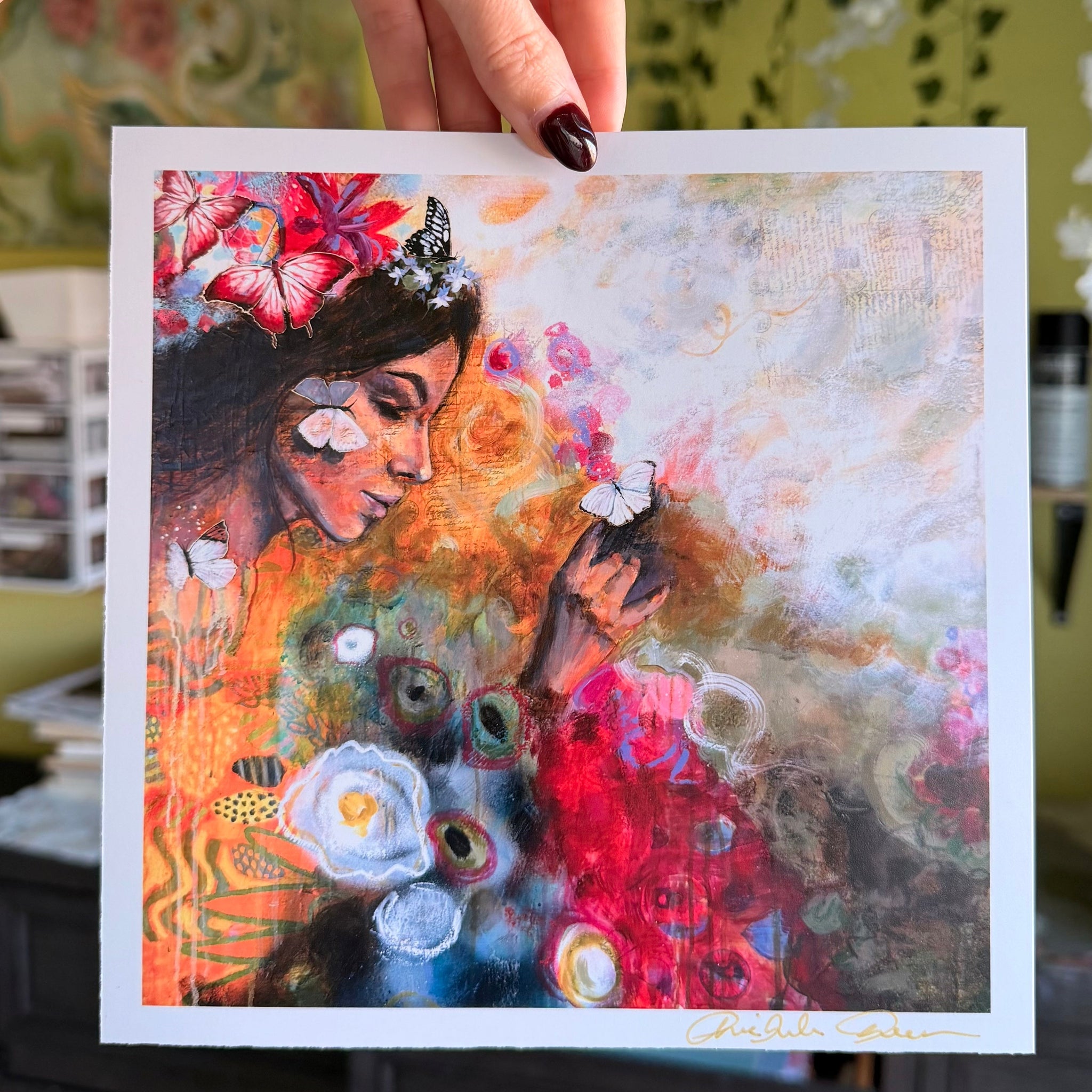 Hand holding a colorful painting of a woman with flowers