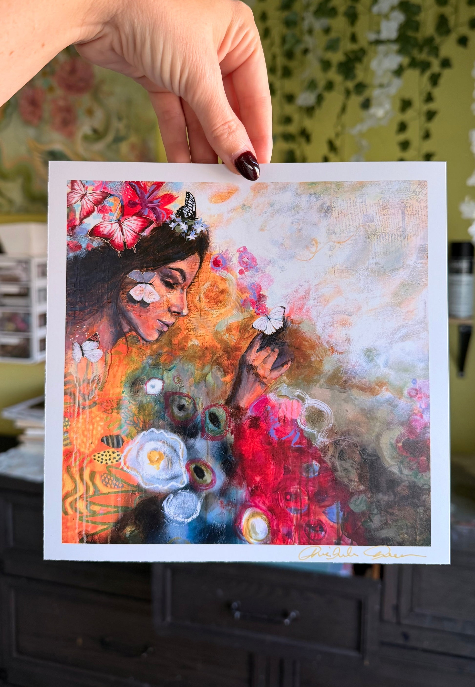 Hand holding a colorful painting of a woman with flowers