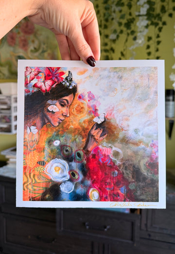 Hand holding a colorful painting of a woman with flowers