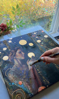 Artistic depiction of a woman with celestial elements on a canvas, held by a hand with a brush.
