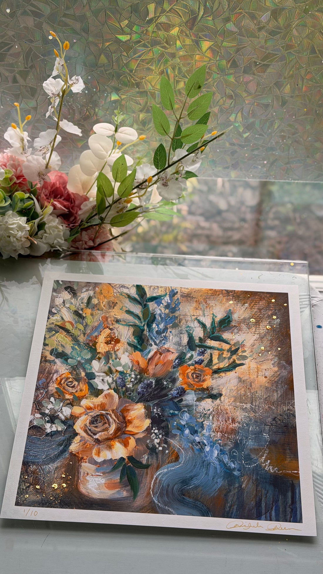 Floral painting held by a person with a blurred indoor background
