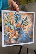 Floral painting held by a person with a blurred indoor background