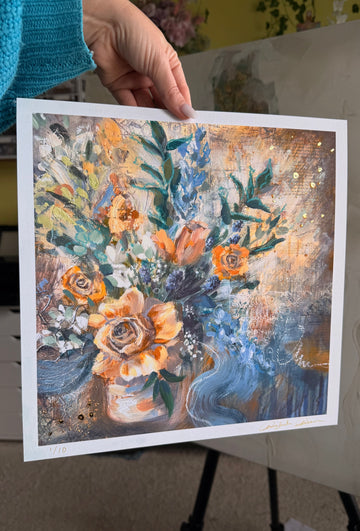 Floral painting held by a person with a blurred indoor background