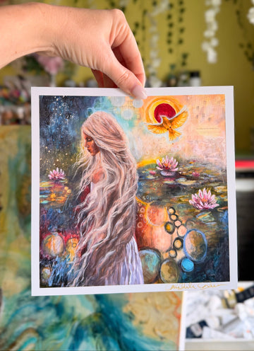 Hand holding a colorful painting of a woman with long hair by a pond with flowers.