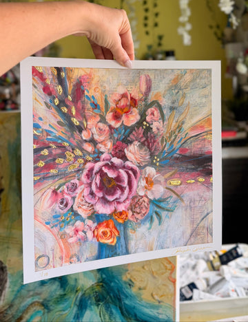 Hand holding a colorful floral art print against a blurred indoor background