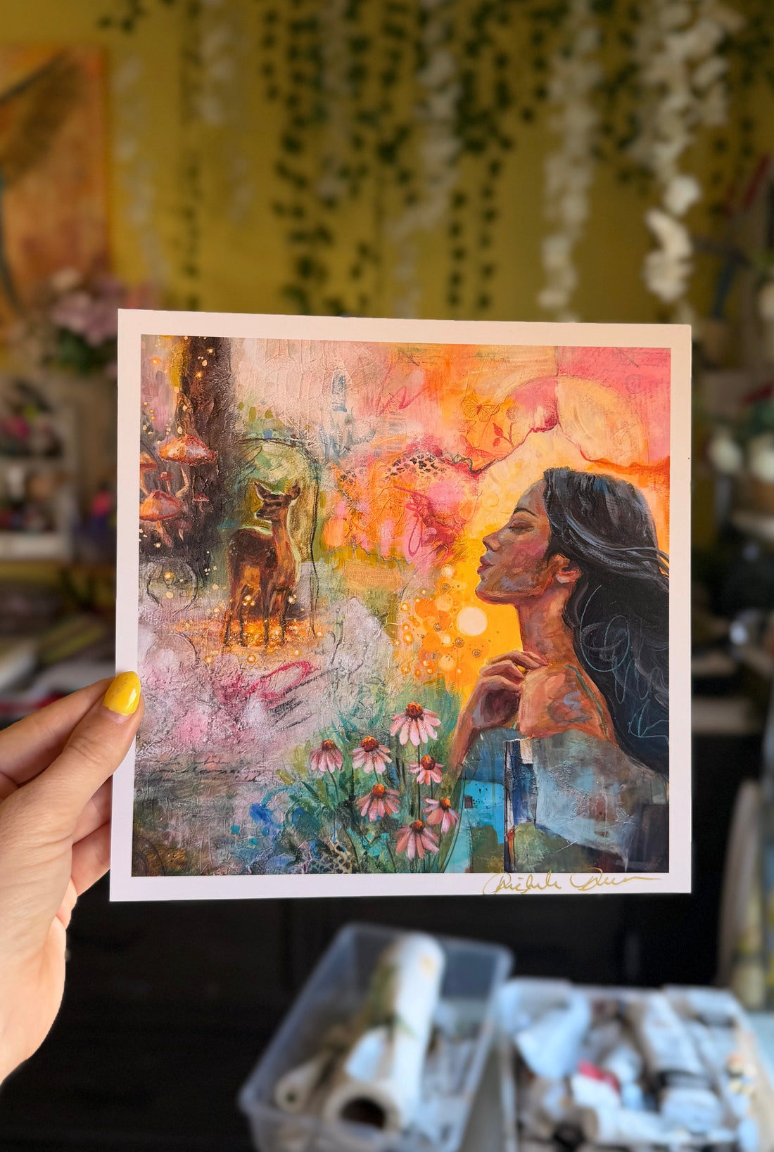 Art print of a woman and deer in a colorful landscape held by a person.