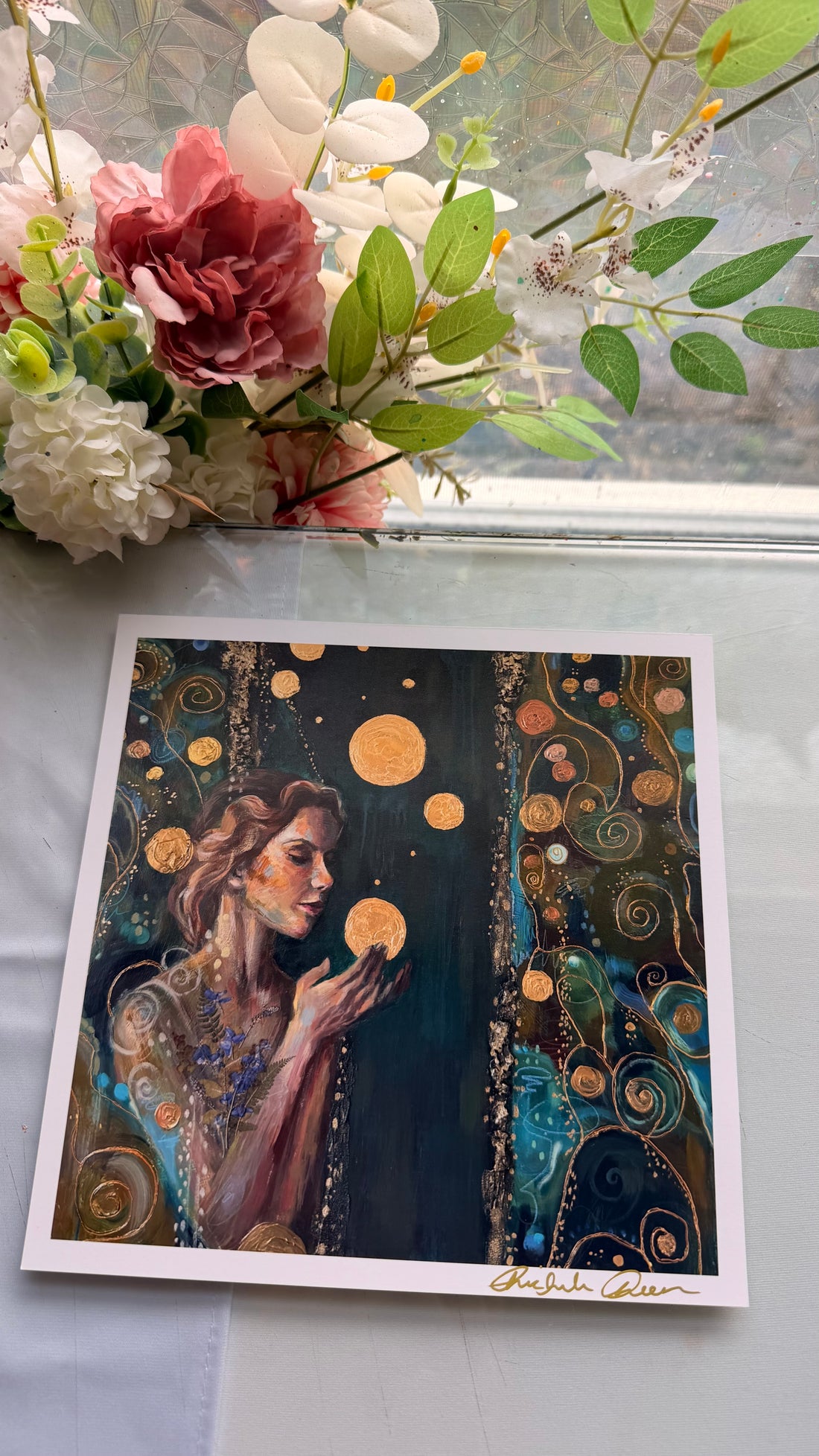 Artistic depiction of a woman holding celestial bodies, held by a hand with green nail polish.