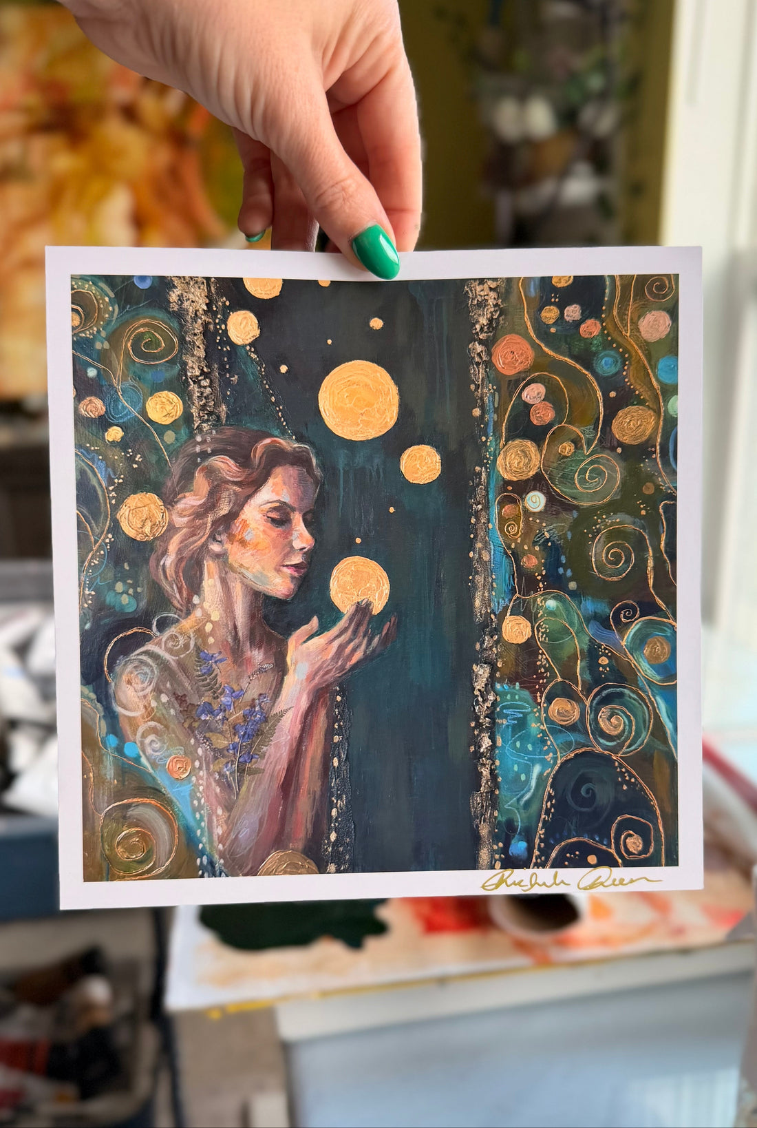 Artistic depiction of a woman holding celestial bodies, held by a hand with green nail polish.