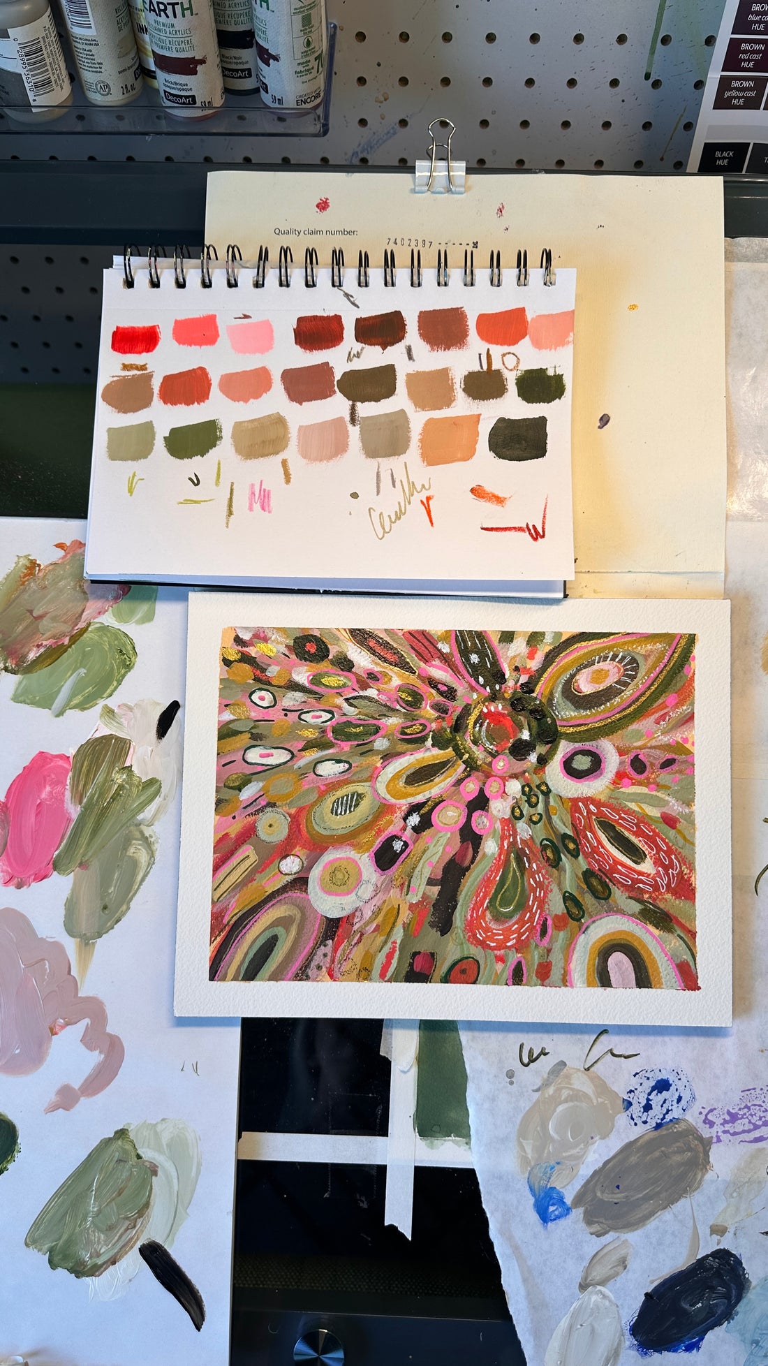 Colorful abstract artwork held by a hand on a light surface with flowers in the background