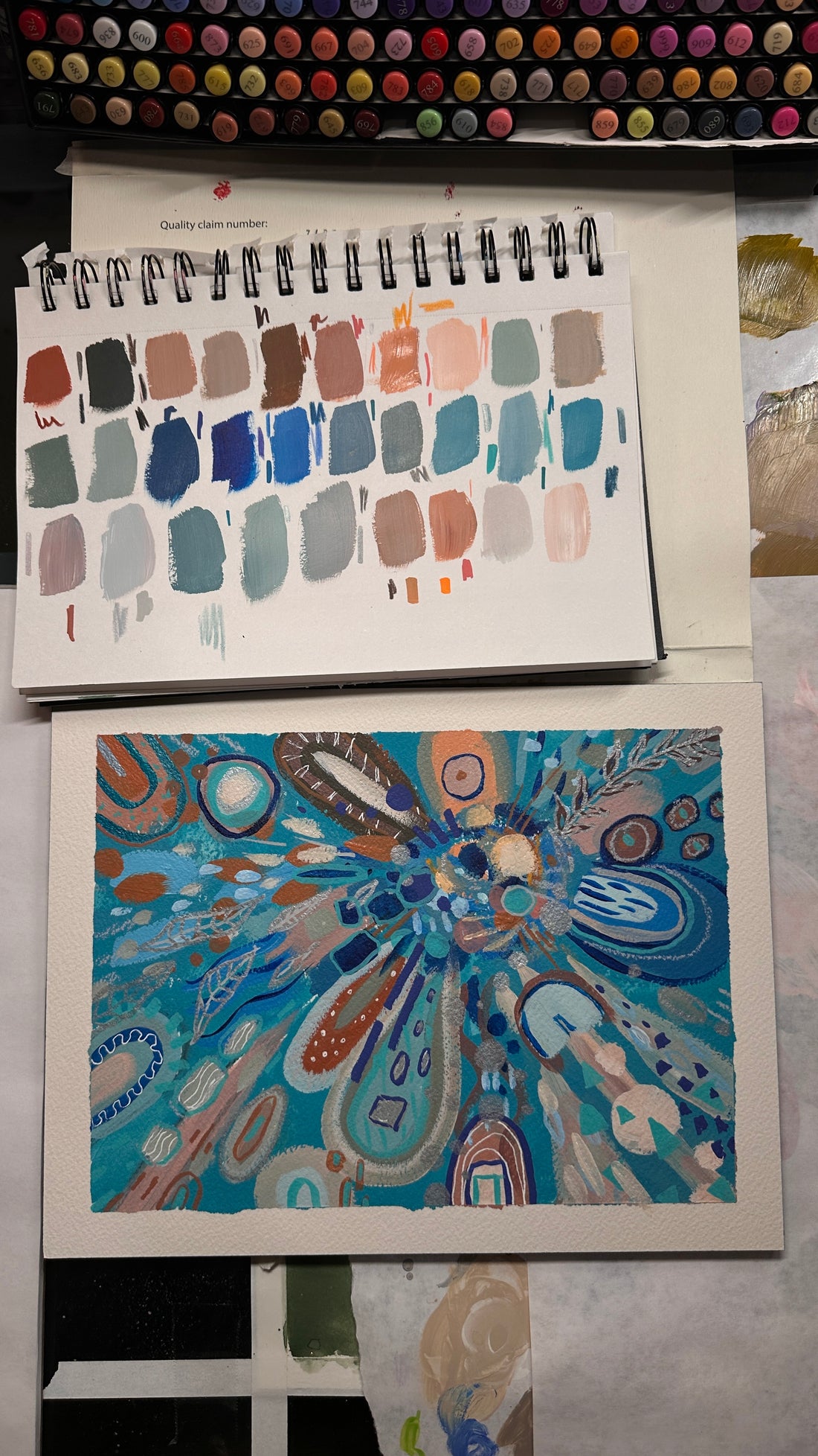 Colorful abstract artwork held by a hand on a reflective surface with flowers in the background