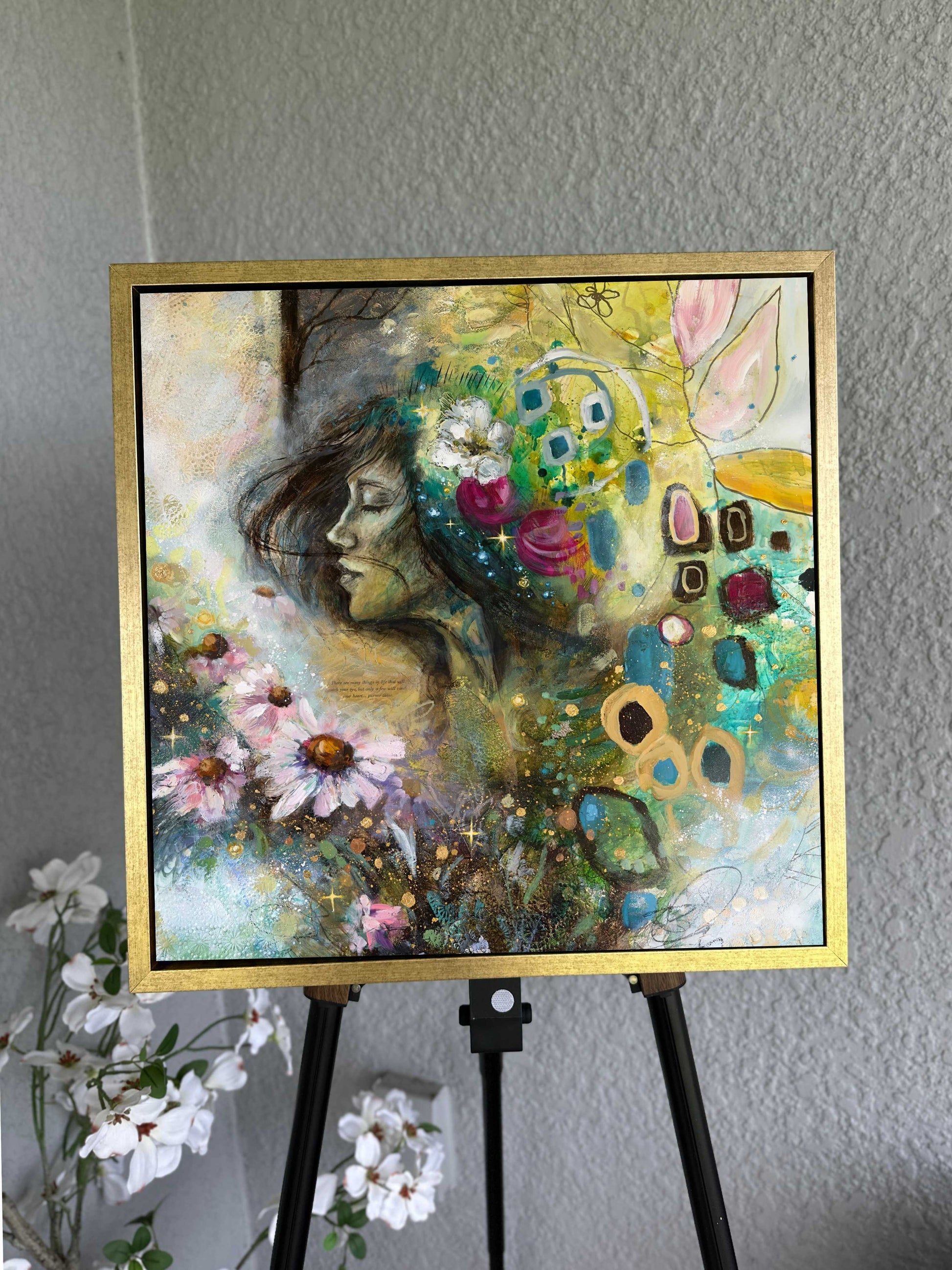 Colorful abstract painting of a woman with flowers on an easel against a gray wall.