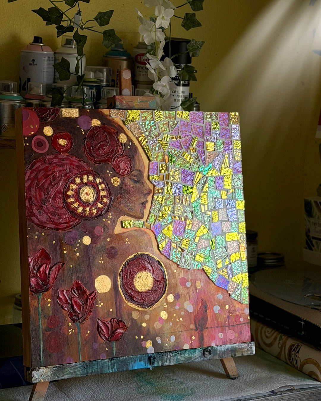 Colorful mosaic art piece on an easel with various materials in the background.