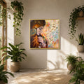 A framed abstract art print featuring a woman in profile with glowing tree-like roots and colorful floral elements, displayed on a beige wall in a sunlit room with potted plants.